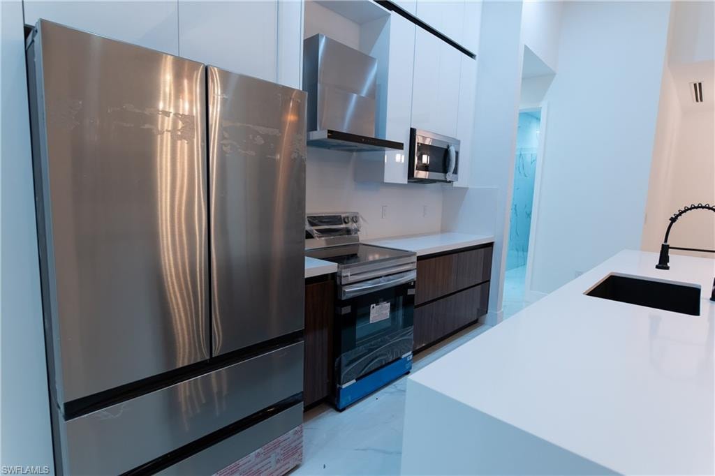 Kitchen featuring white cabinetry, sink, stainless steel appliances, and wall chimney exhaust hood