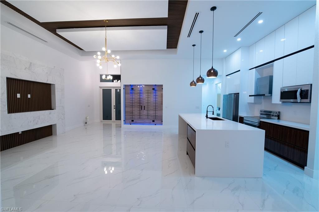 Kitchen featuring dark brown cabinetry, sink, decorative light fixtures, appliances with stainless steel finishes, and an island with sink