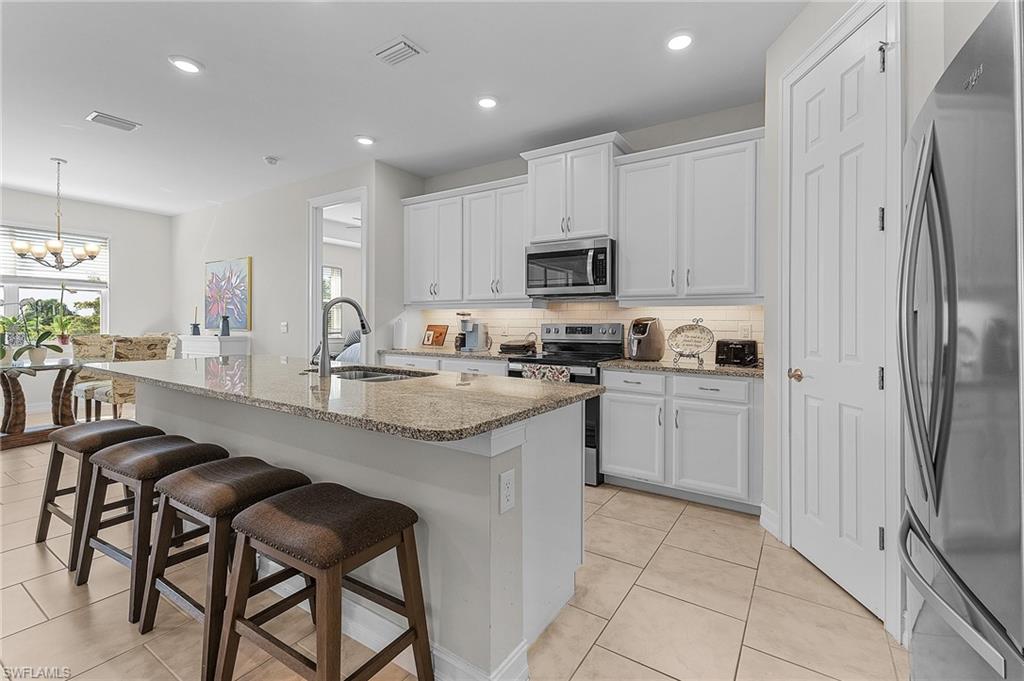 Kitchen featuring white cabinetry, sink, stainless steel appliances, and an island with sink