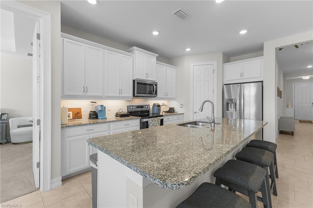 Kitchen featuring a kitchen island with sink, sink, white cabinets, and appliances with stainless steel finishes