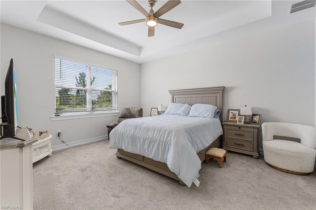 Bedroom featuring ceiling fan, light colored carpet, and a tray ceiling