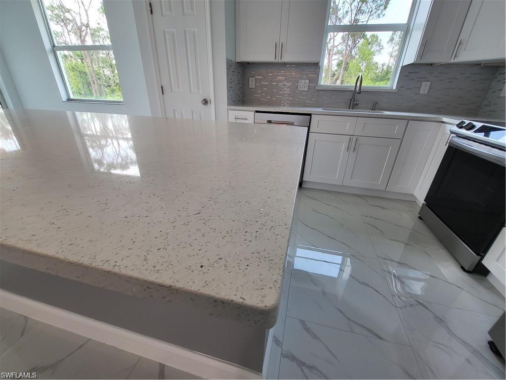 Kitchen with electric stove, sink, white cabinetry, light stone counters, and tasteful backsplash