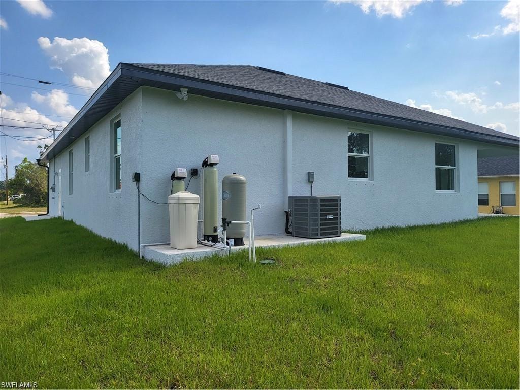 Rear view of property featuring central AC unit and a lawn