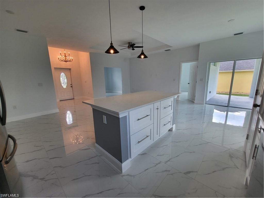 Kitchen featuring hanging light fixtures, a center island, ceiling fan with notable chandelier, and white cabinets