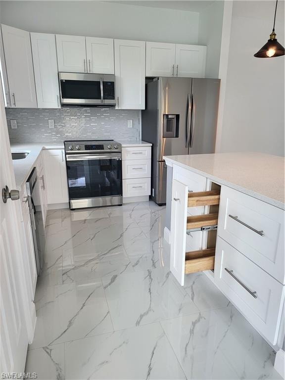Kitchen featuring hanging light fixtures, decorative backsplash, stainless steel appliances, and white cabinets