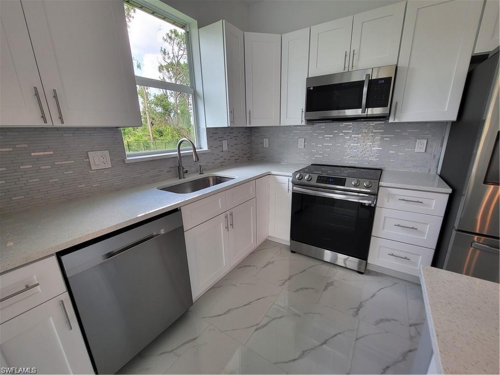 Kitchen with white cabinetry, stainless steel appliances, sink, and tasteful backsplash