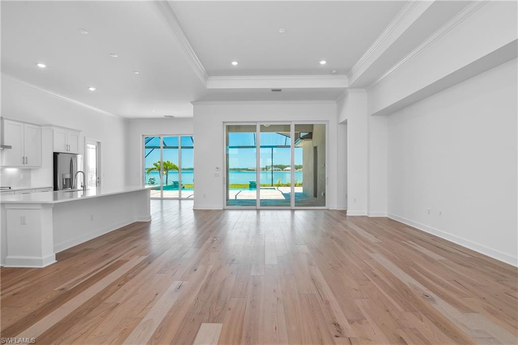 Unfurnished living room with a raised ceiling, crown molding, sink, and light hardwood / wood-style floors