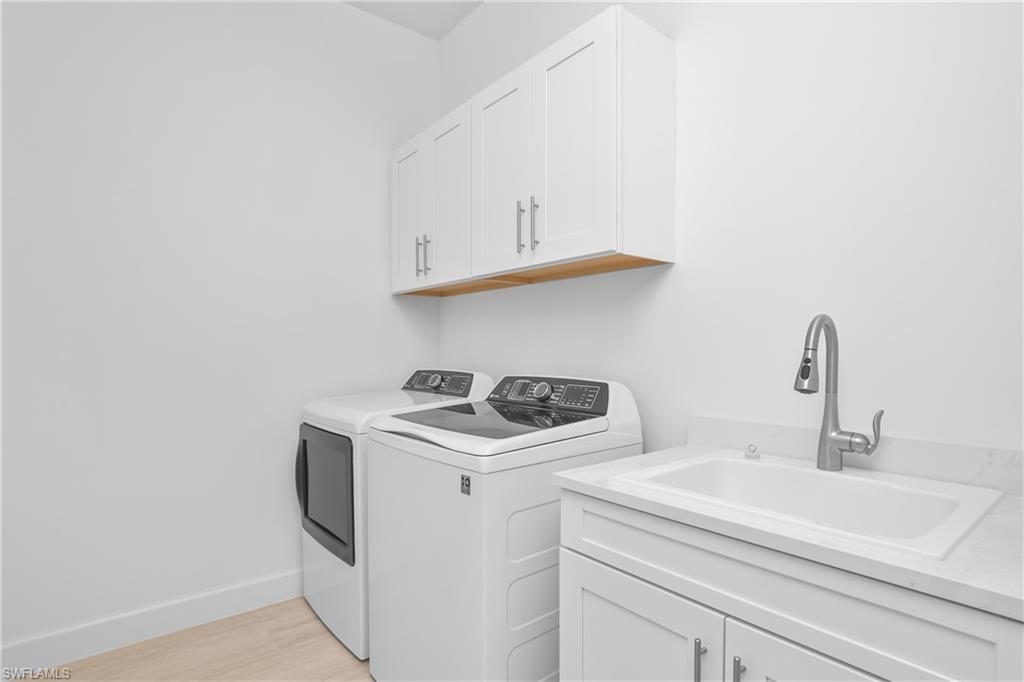 Laundry room with cabinets, washer and dryer, sink, and light wood-type flooring