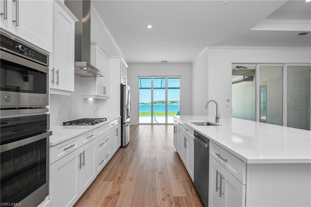 Kitchen with stainless steel refrigerator with ice dispenser, a water view, a center island with sink, wall chimney range hood, and white cabinets