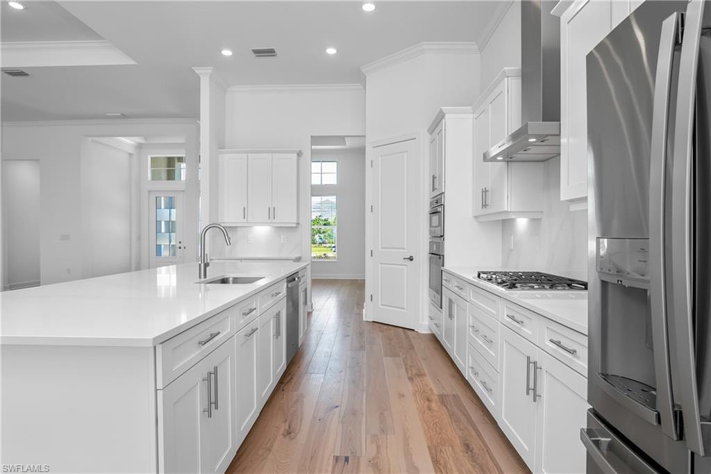 Kitchen with sink, white cabinetry, appliances with stainless steel finishes, a kitchen island with sink, and wall chimney range hood