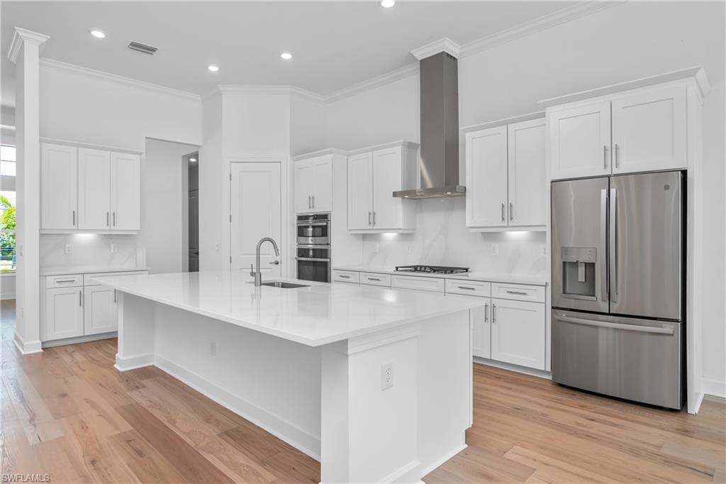Kitchen with white cabinetry, appliances with stainless steel finishes, and wall chimney exhaust hood