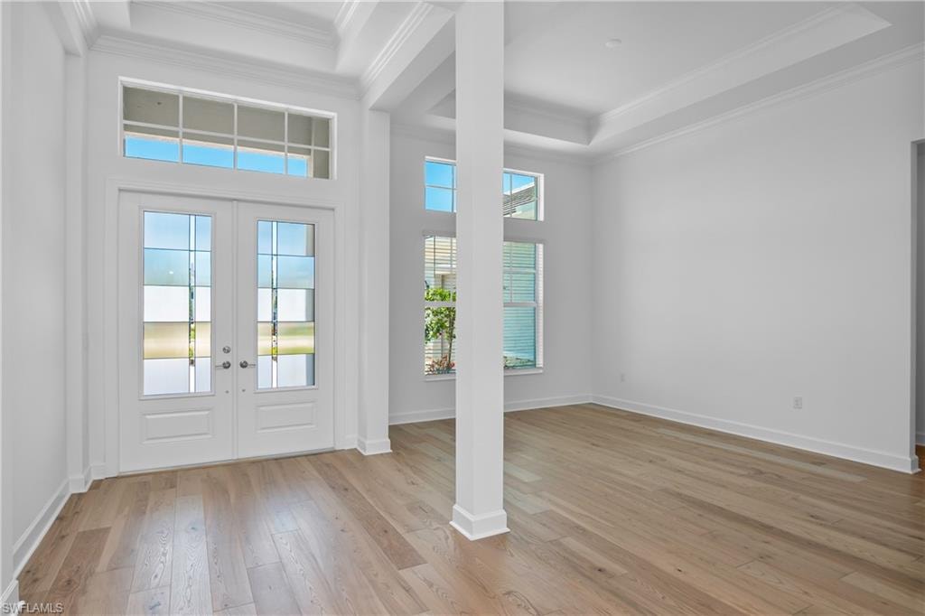 Entrance foyer with crown molding, a tray ceiling, french doors, and light wood-type flooring