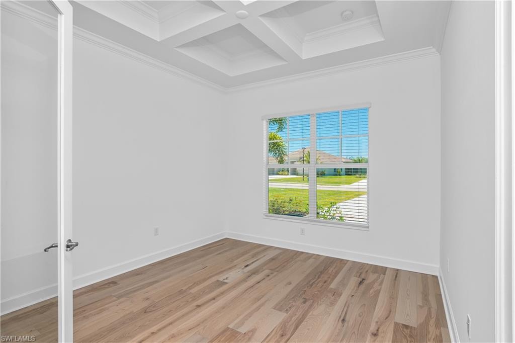 Empty room with beam ceiling, crown molding, coffered ceiling, and light hardwood / wood-style floors