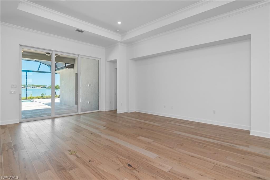 Unfurnished room featuring ornamental molding, a water view, light wood-type flooring, and a tray ceiling