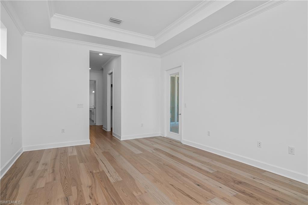 Spare room with ornamental molding, a tray ceiling, and light wood-type flooring