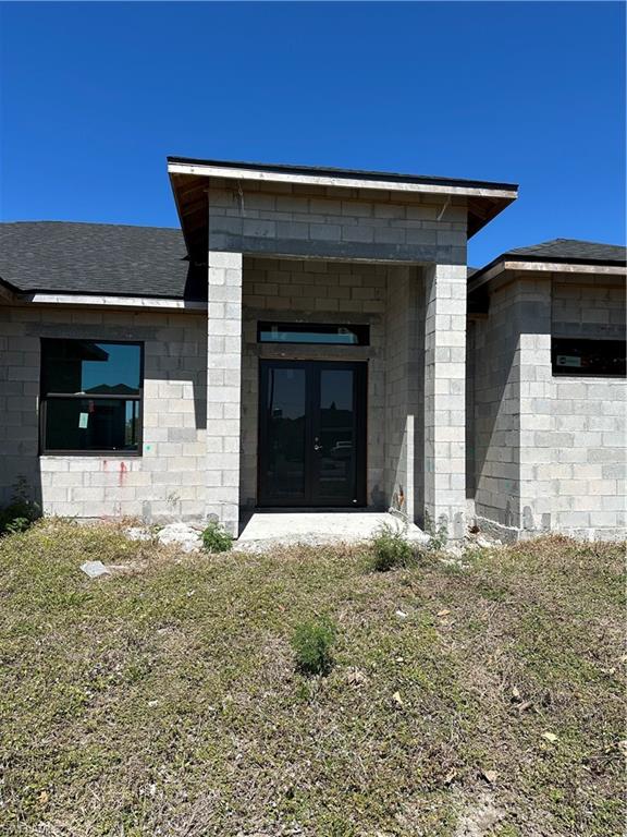 Entrance to property featuring a shingled roof, stucco siding, and french doors