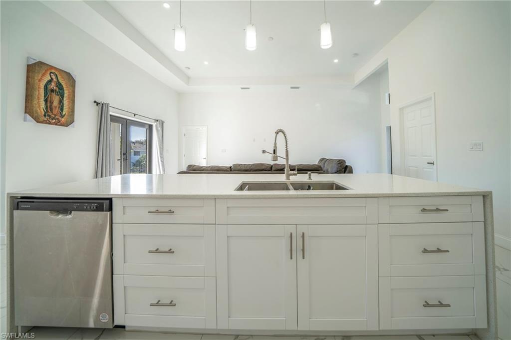 Kitchen with dishwasher, white cabinetry, sink, hanging light fixtures, and french doors