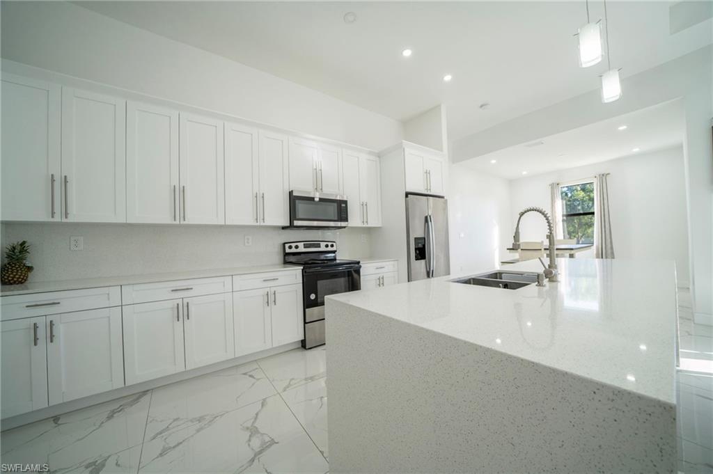 Kitchen with decorative light fixtures, white cabinetry, an island with sink, sink, and stainless steel appliances
