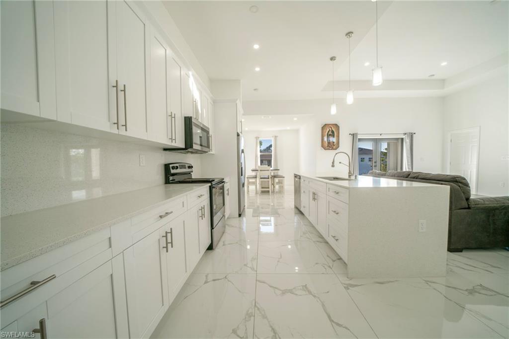Kitchen featuring sink, appliances with stainless steel finishes, pendant lighting, a kitchen island with sink, and white cabinets