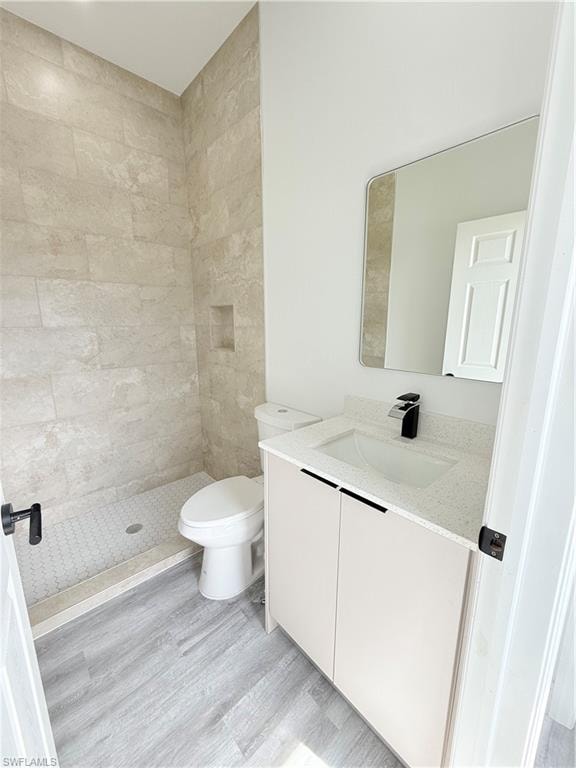 Bathroom with vanity, wood-type flooring, toilet, and tiled shower