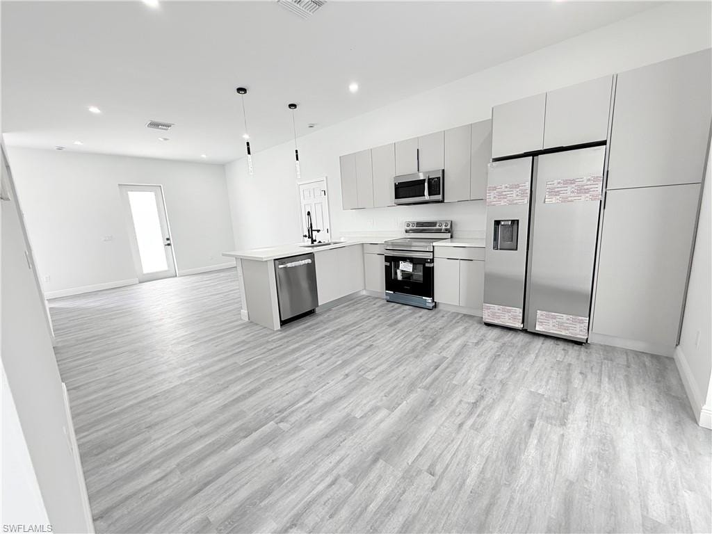 Kitchen featuring gray cabinetry, decorative light fixtures, appliances with stainless steel finishes, kitchen peninsula, and light hardwood / wood-style floors