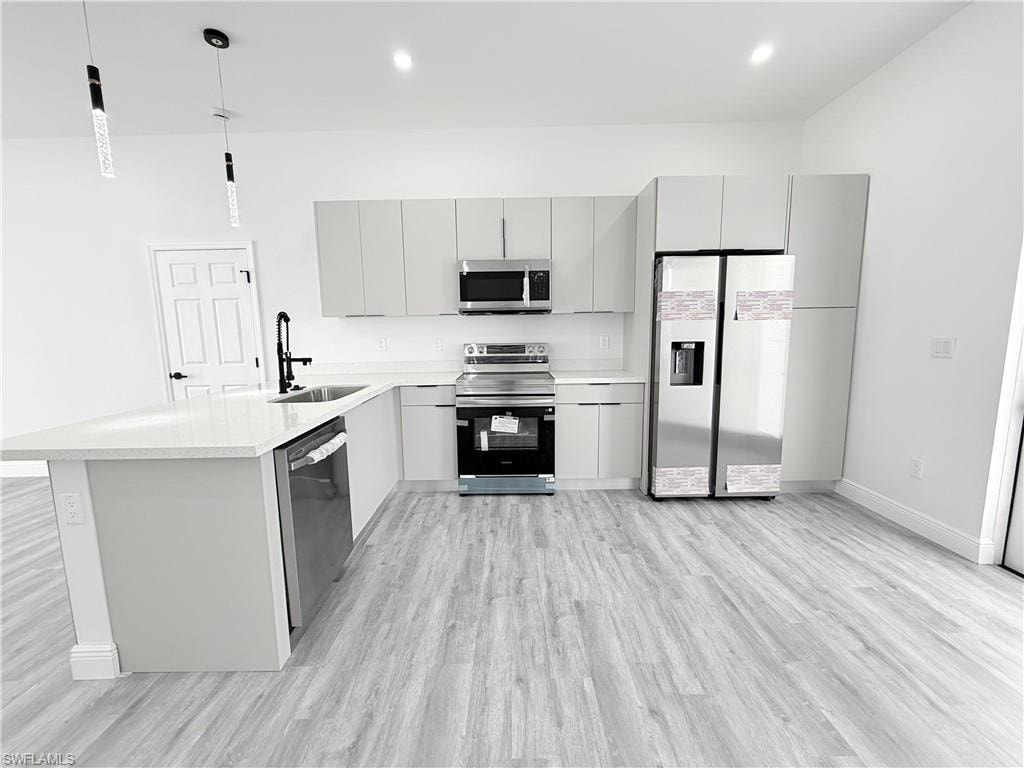 Kitchen with pendant lighting, sink, appliances with stainless steel finishes, gray cabinetry, and light wood-type flooring