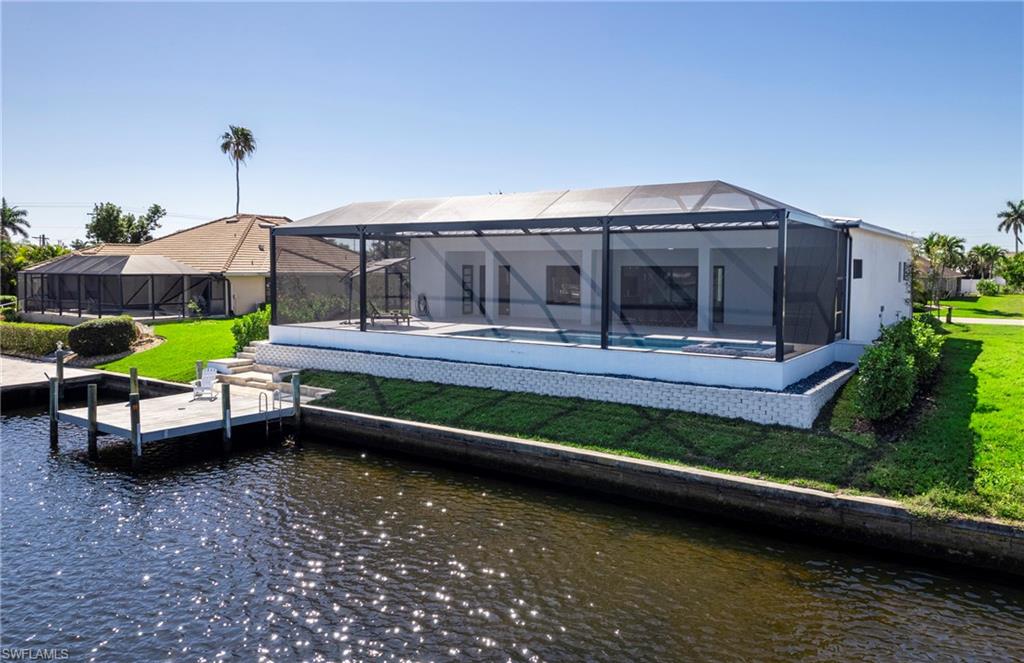 Rear view of house with glass enclosure, a yard, an outdoor pool, and a water view