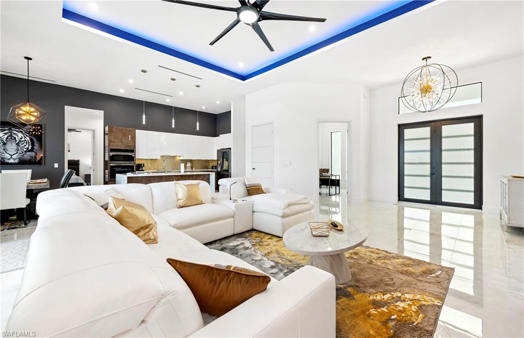 Living room featuring a raised ceiling, marble finish floor, ceiling fan with notable chandelier, a high ceiling, and baseboards