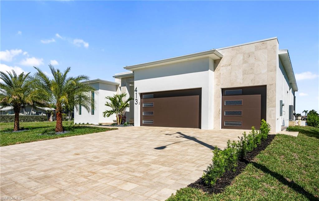 Modern home with a garage, decorative driveway, a front lawn, and stucco siding