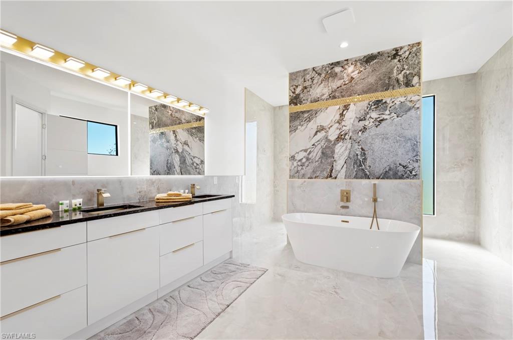 Bathroom with a freestanding bath, double vanity, marble finish floor, tile walls, and a sink
