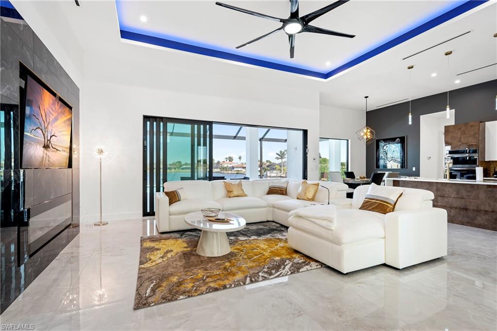 Living area with marble finish floor, a ceiling fan, a tray ceiling, and a towering ceiling