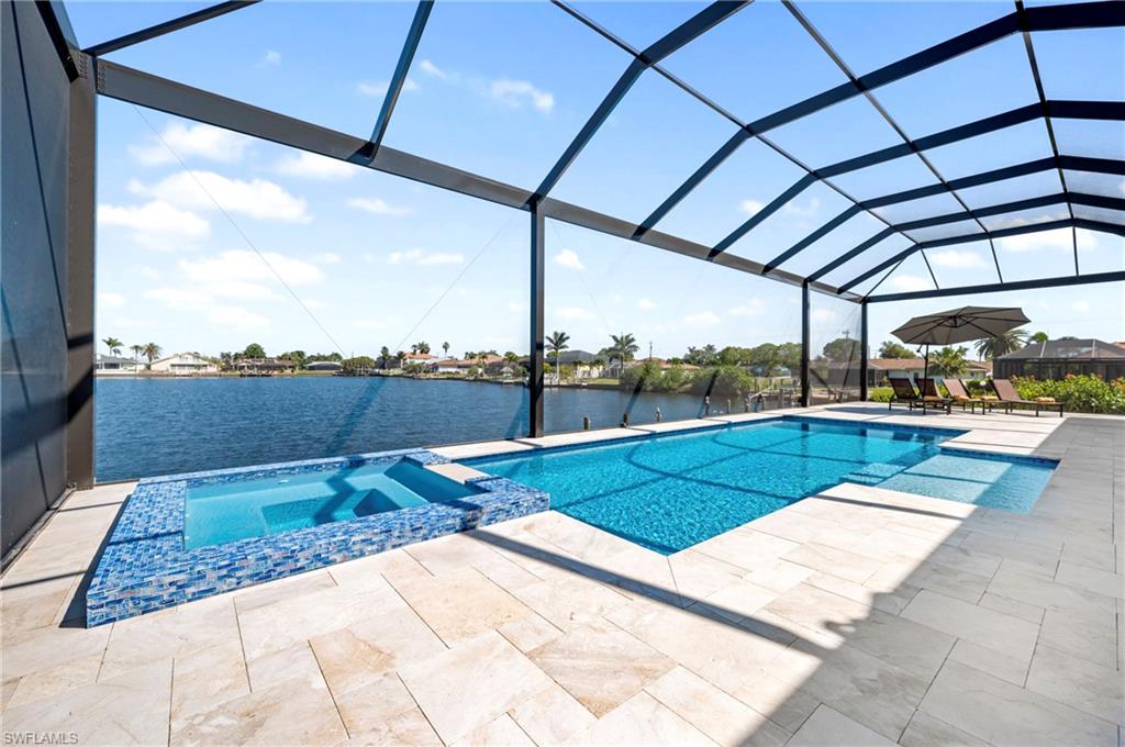View of pool featuring a lanai, a patio area, a water view, and a pool with connected hot tub