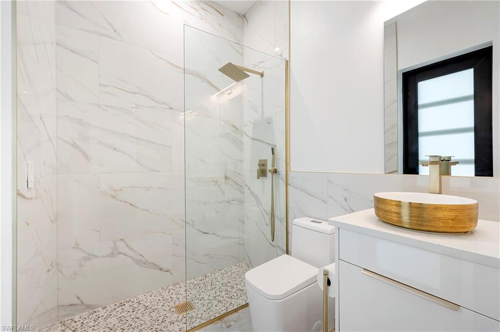 Bathroom featuring a marble finish shower, toilet, tile walls, and vanity