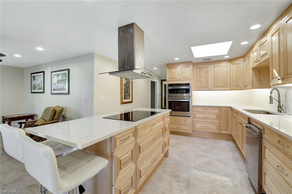 Kitchen featuring stainless steel appliances, island range hood, sink, a kitchen bar, and light brown cabinetry