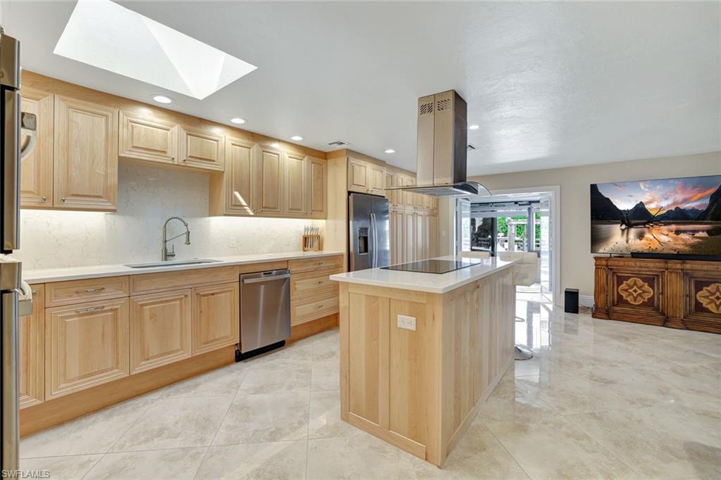 Kitchen with appliances with stainless steel finishes, light brown cabinetry, island exhaust hood, a kitchen island, and sink