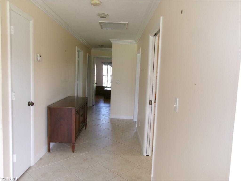 Hallway with light tile patterned floors, ornamental molding, and baseboards