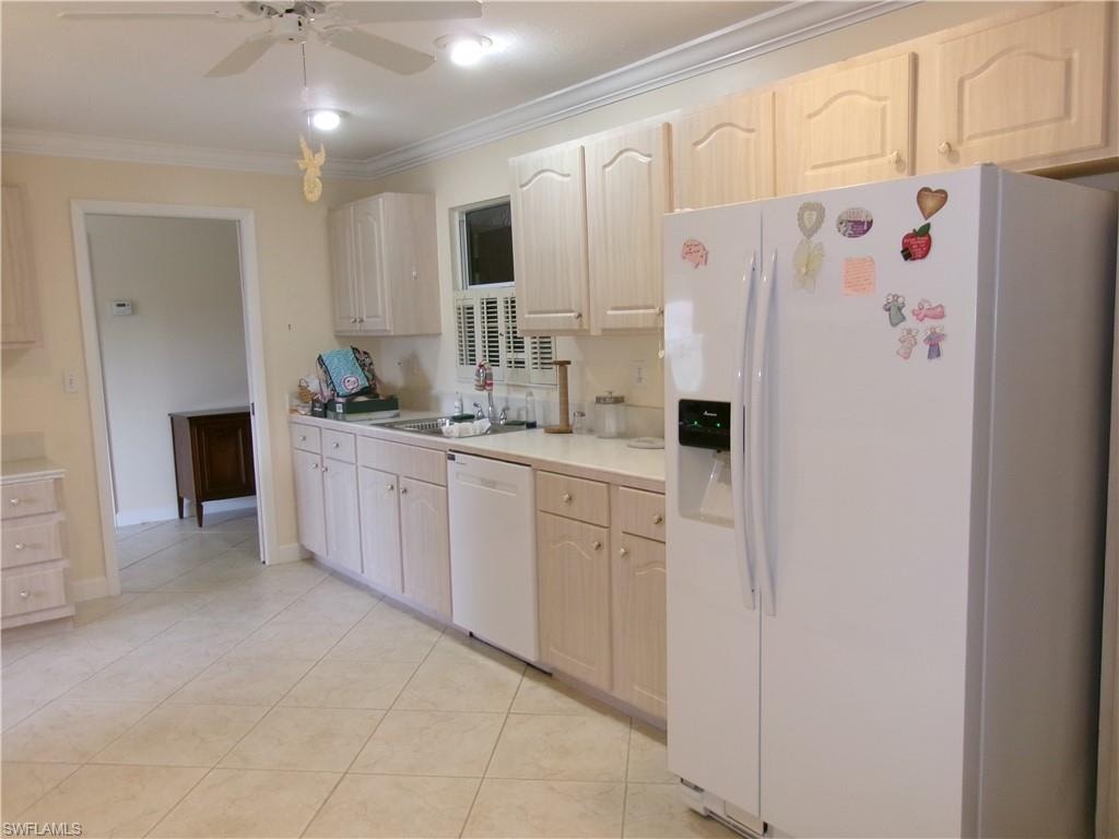 Kitchen featuring light tile patterned flooring, white appliances, a sink, light countertops, and ornamental molding