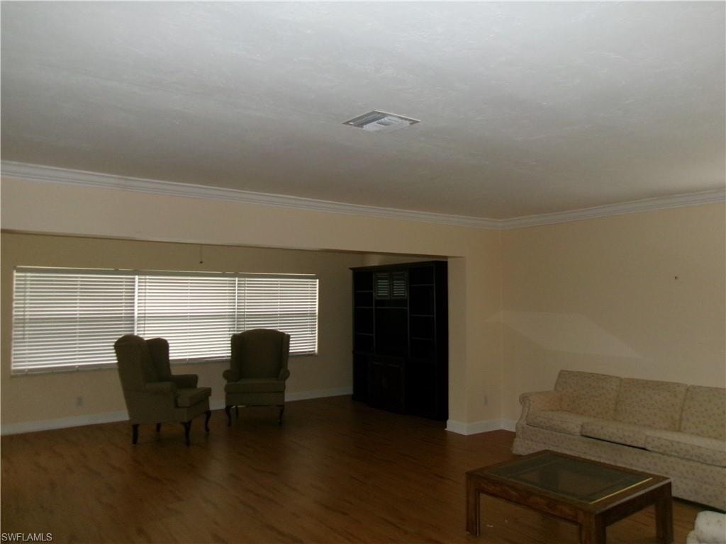 Living room with ornamental molding, dark wood-style flooring, visible vents, and baseboards