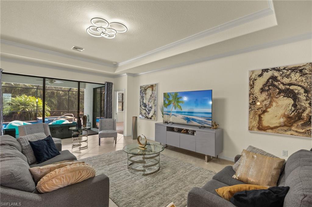 Living room featuring a raised ceiling, light tile patterned floors, a textured ceiling, and ornamental molding
