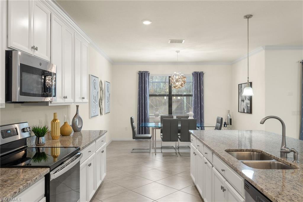 Kitchen with hanging light fixtures, sink, light stone counters, appliances with stainless steel finishes, and white cabinets