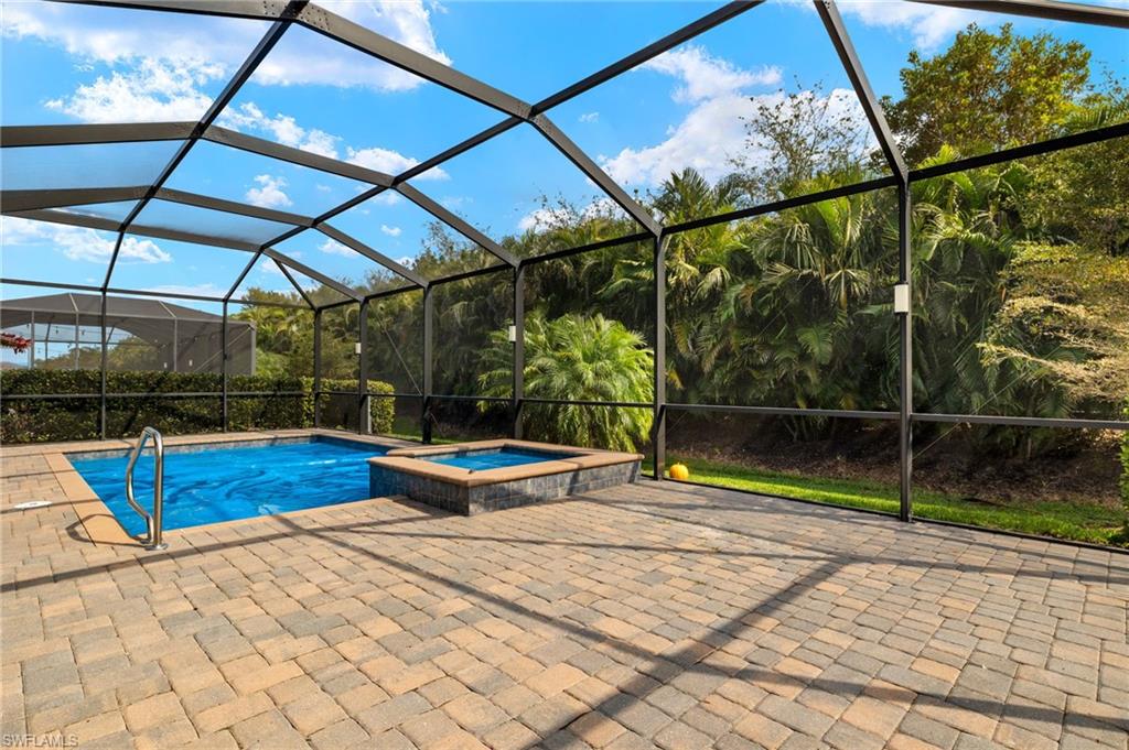 View of swimming pool with an in ground hot tub, glass enclosure, and a patio area