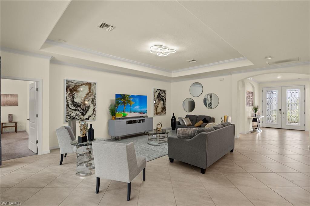 Living room featuring french doors, light tile patterned floors, crown molding, and a raised ceiling