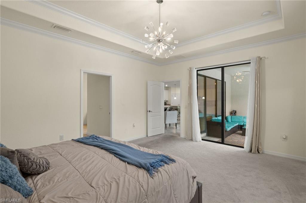 Carpeted bedroom featuring ornamental molding, access to exterior, a chandelier, and a raised ceiling