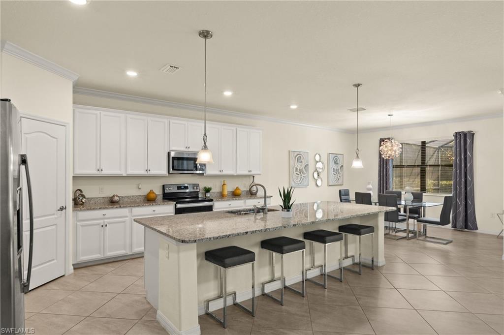 Kitchen with a center island with sink, sink, decorative light fixtures, stainless steel appliances, and white cabinets