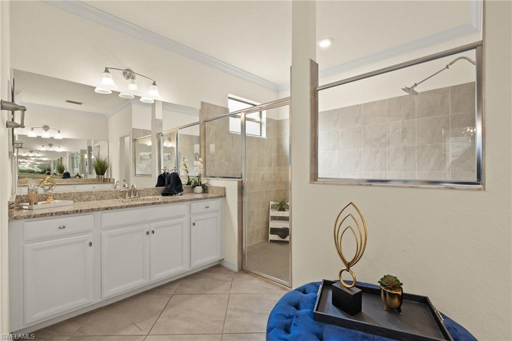Bathroom featuring vanity, a shower with shower door, ornamental molding, and tile patterned flooring