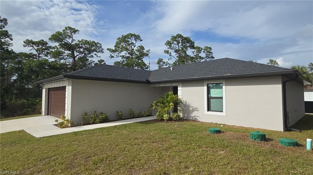 View of side of property featuring a lawn, stucco siding, concrete driveway, and a garage
