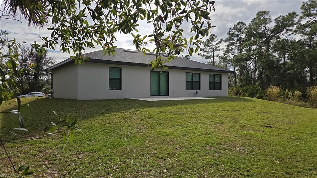 Rear view of property with a patio, a yard, stucco siding, and a shingled roof