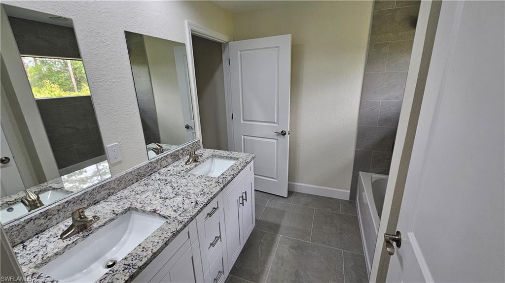 Bathroom with double vanity, baseboards, tile patterned flooring, and a tub