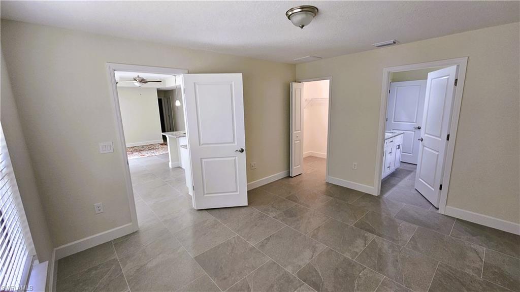 Unfurnished bedroom with a spacious closet, baseboards, ensuite bathroom, and a closet