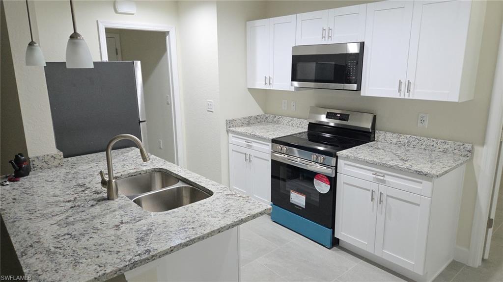 Kitchen featuring stainless steel appliances, pendant lighting, white cabinets, and light stone counters